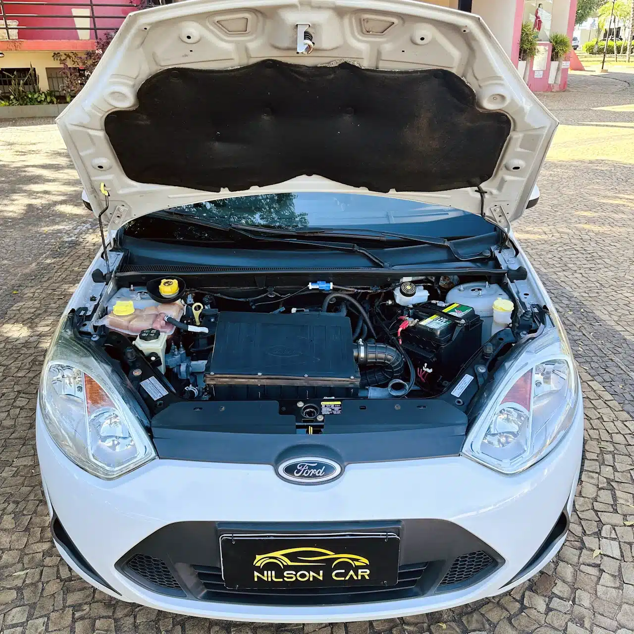 2013 Ford Fiesta Sedan 16 M Flex Branco - engine - Nilson Car White Ford with hood up, showing the engine bay and components (battery on the right, coolant reservoir on the left).