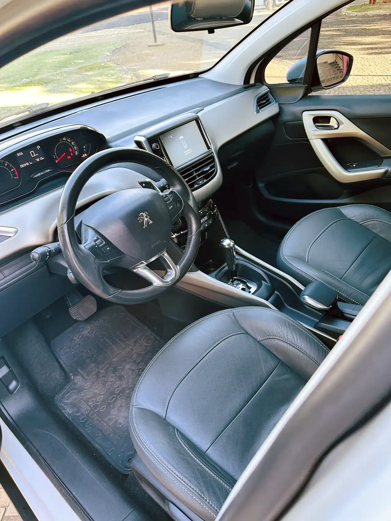 2016 PEUGEOT 2008 16 ALLURE BRANCA - front_seat - Nilson Car Interior of a car showing the driver’s seat, steering wheel with a Peugeot logo, and center console with a touchscreen display