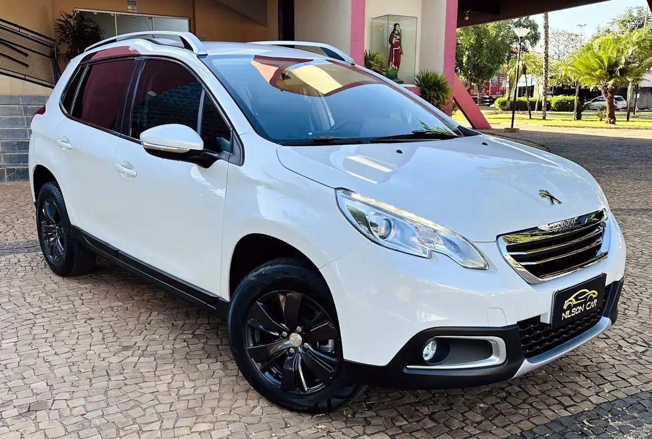 2016 PEUGEOT 2008 16 ALLURE BRANCA - front_side - Nilson Car White Peugeot SUV parked on a stone-paved lot, front three-quarter view with black alloy wheels and roof rails.