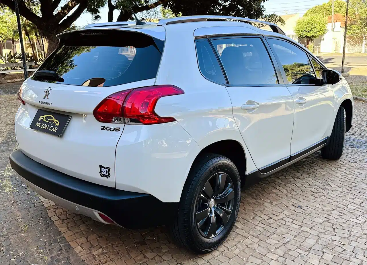2016 PEUGEOT 2008 16 ALLURE BRANCA - rear_side - Nilson Car Rear three-quarter view of a white Peugeot 2008 SUV parked on a cobblestone area with trees in the background.