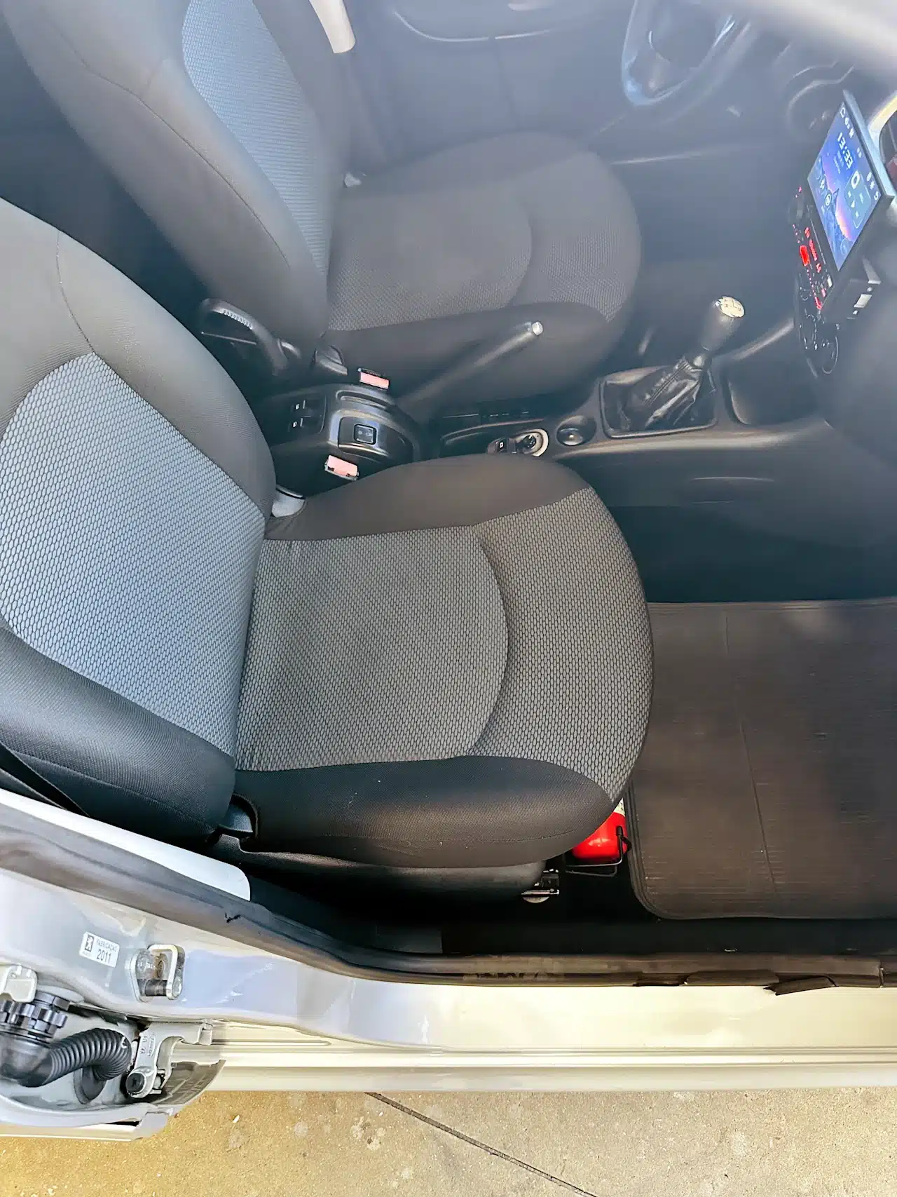 Peugeot_ 207_ 2011_2012_Prata-front_seat - Nilson Car Interior of a car showing the front seats (gray fabric), manual gear shift, center console with controls, and a touchscreen infotainment display on the dash.