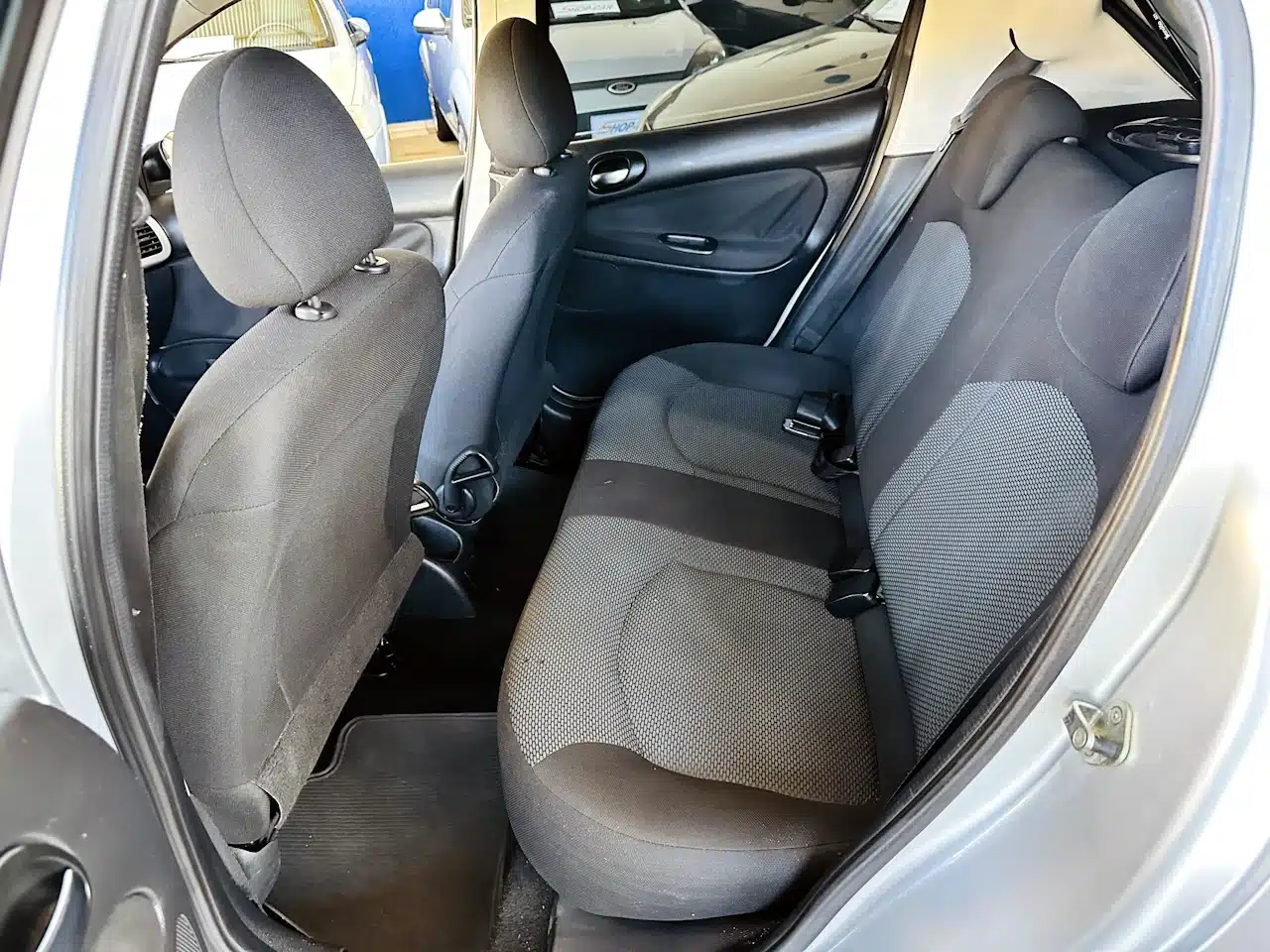 Peugeot_ 207_ 2011_2012_Prata-rear_seat - Nilson Car Interior view of a compact car showing gray cloth rear seats with headrests and a door panel on the right side