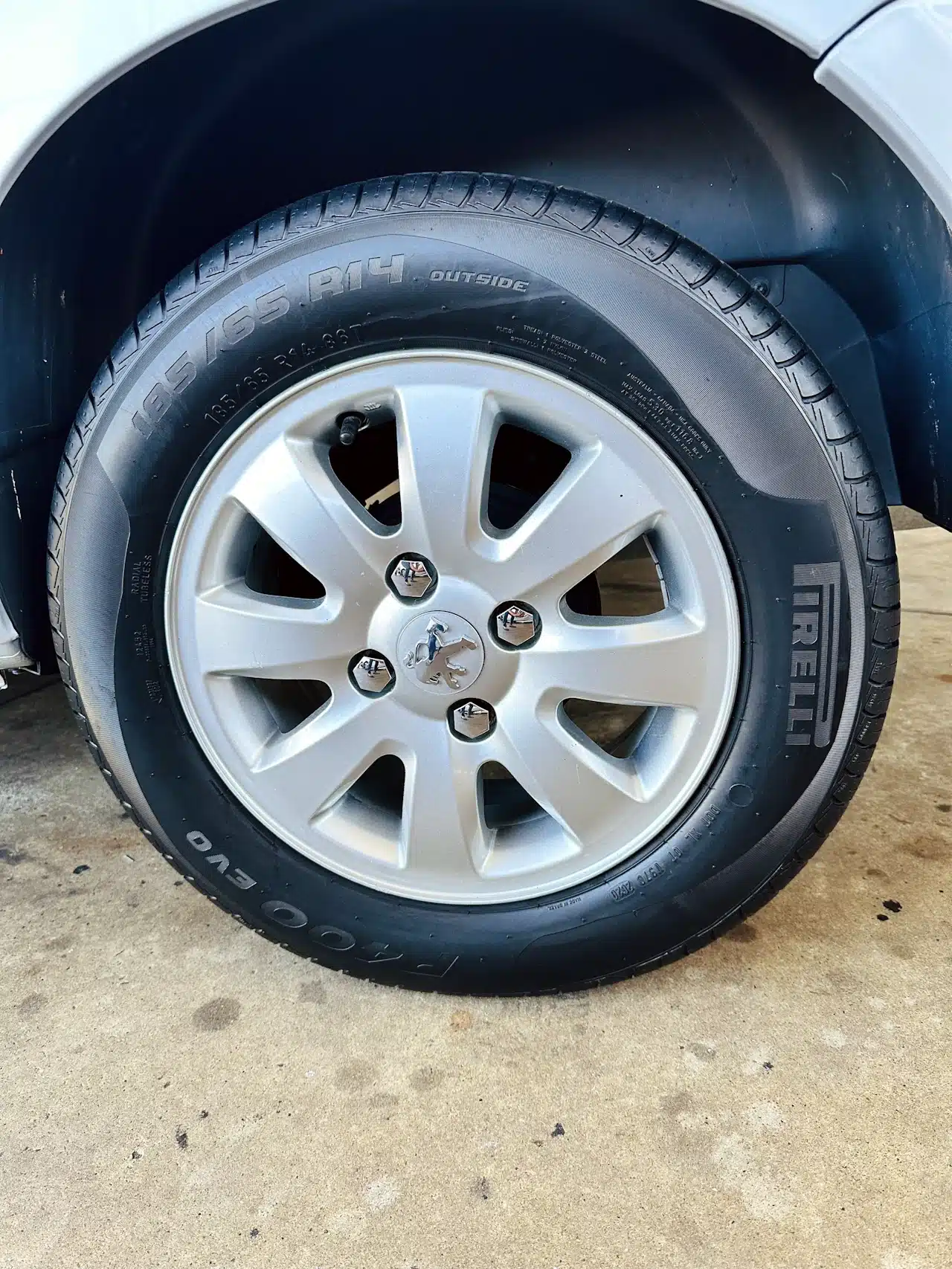 Peugeot_ 207_ 2011_2012_Prata-tire - Nilson Car Silver alloy wheel with a black Pirelli tire (195/65 R14) mounted on a car, resting on a concrete surface.